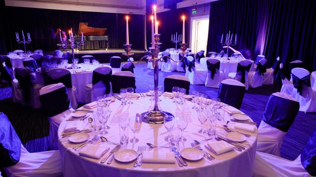Round tables set for dinner in The Studio with a grand piano on the stage with blue/purple lighting