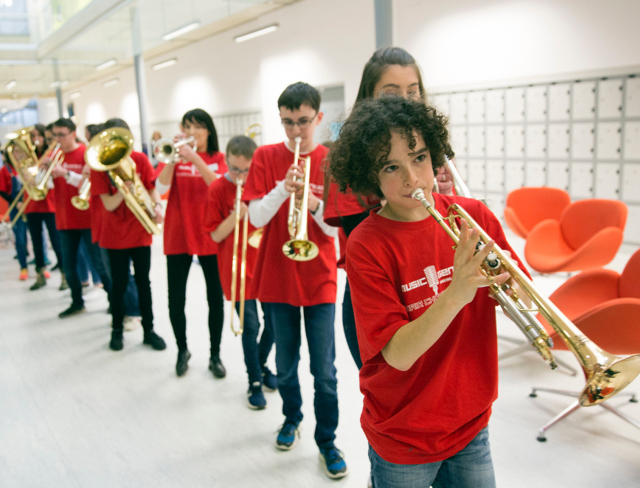 Girls and boys taking part in a Music Generation initiative dressed in red playing brass instruments